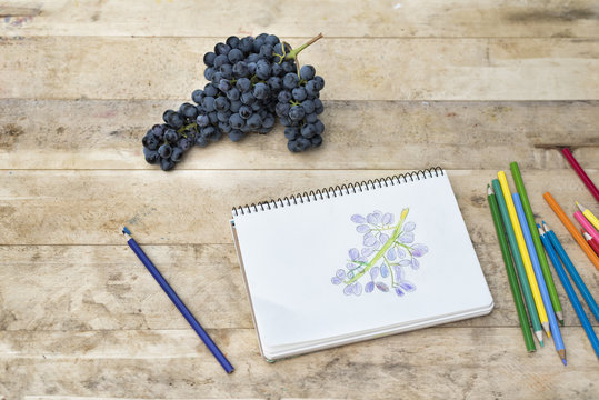 Children's drawing, grapes and colored pencils. Wooden table. Top view