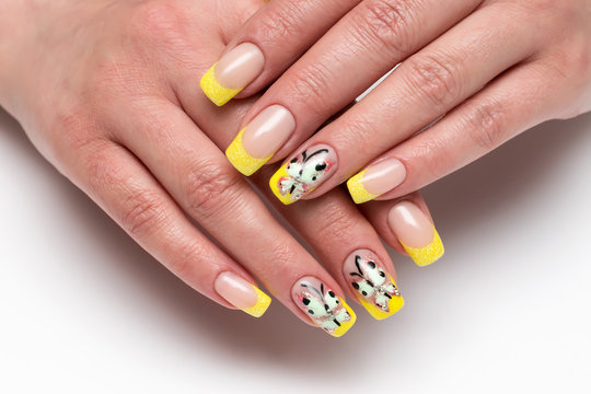 French yellow shiny manicure with painted butterflies and crystals on long, square nails on a white background close-up
