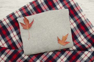 Gray sweater on checkered  plaid and autumn leaves. Fashionable concept