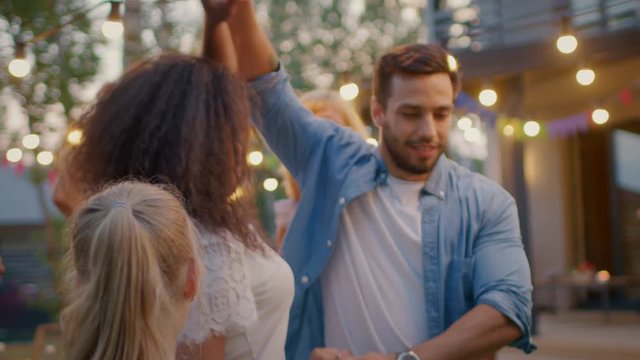 Romantic Couple Dances Together with Group of Friends at the Garden Party Celebration. Beautiful and Handsome People Having Fun one at the House Backyard on one Summer Evening. In Slow Motion.
