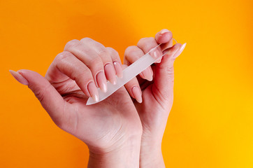Woman doing a manicure with a glass nail file on an orange background