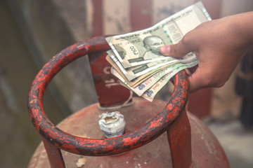Man holding LPG gas cylinder and Indian rupee notes