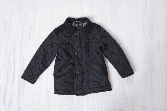 Black Kids Quilted Jacket On Wooden Background. Fashionable Concept