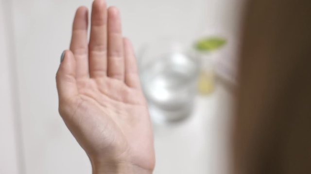 Close up of woman's hand holding white pills in hand and taking glass of water