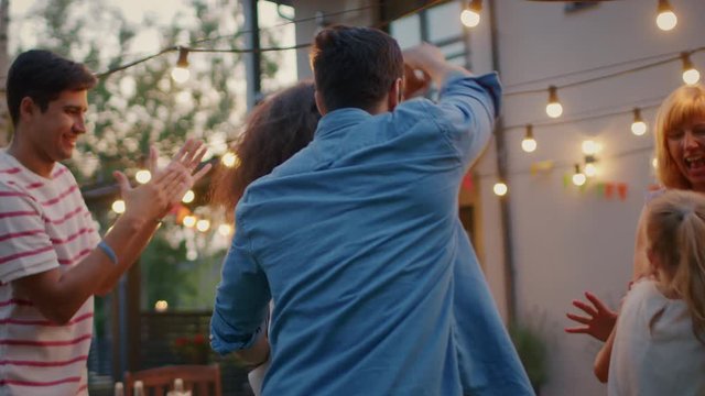 Romantic Couple Dances Together with Group of Friends at the Garden Party Celebration. Beautiful and Handsome People Having Fun one at the House Backyard on one Summer Evening. In Slow Motion.