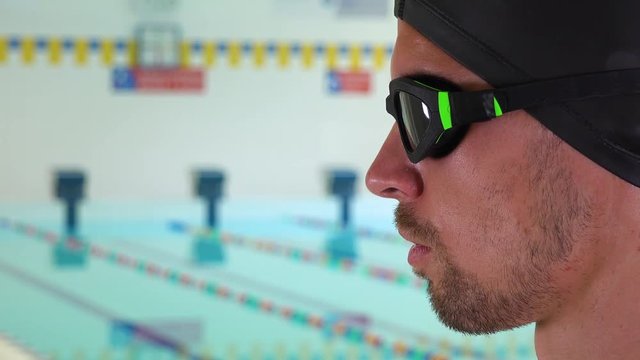 A professional swimmer looks ahead and takes deep breaths at an indoor pool - face closeup from the side