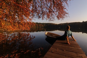 Fototapeta na wymiar Mann sitzt entspannt an einem See mit Steg und Boot im Herbst