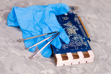 Blue rubber glove and three small metal screwdrivers near pc graphics card with copper radiator on old gray concrete floor