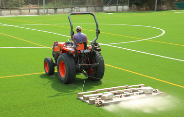 tractor preparando el nuevo césped artificial de un campo de fútbol, poniendo arena - 227986913