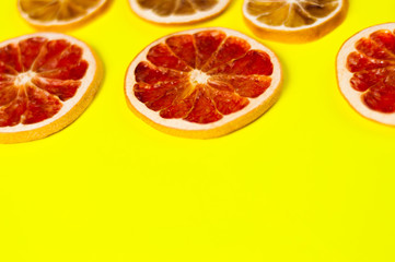 Scattered dried slices grapefruit and lemon on yellow background with copy space