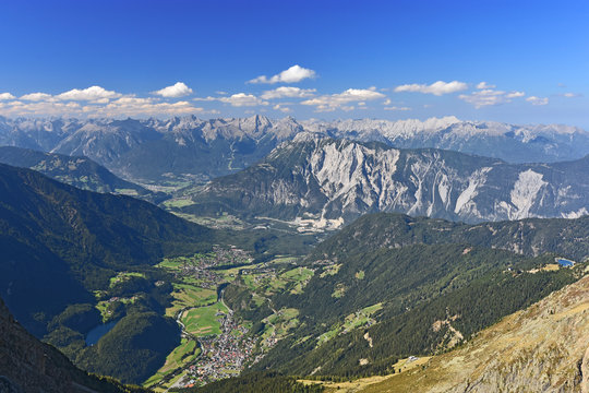 View from the summit of Acherkogel mountain (Tyrol, Austria) at a beautiful day to Inn and Oetztal valley with the village of Oetz. Colorful alpine landscape with rocky mountains, pastures, blue sky.