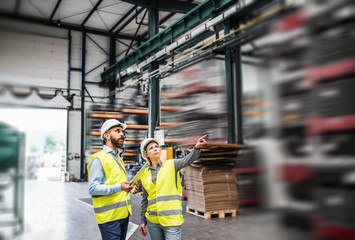 A portrait of an industrial man and woman engineer with tablet in a factory, working.