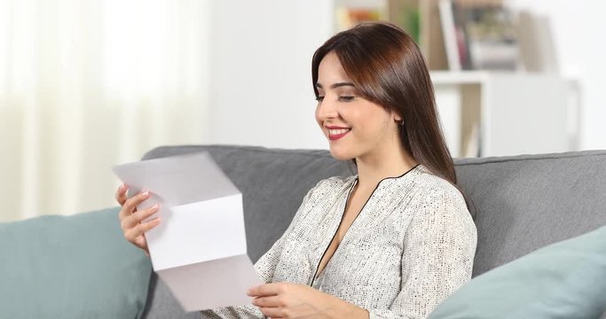 Happy woman reading a letter sitting on a couch at home