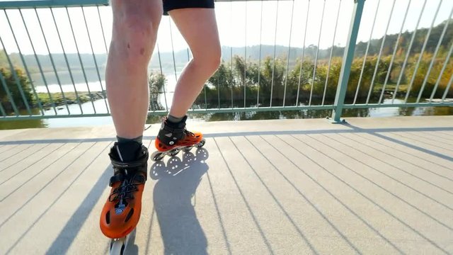 Man legs skating on light asphalt path on lake bridge. Machovo lake range, 9th of October 2018. Outdoor inline skating. Close up view to quick movement of orange hard shell inline boots