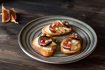 Sandwiches with ricotta, fresh figs, walnuts and honey on rustic wooden board over black backdrop, top view. Bruschetta with figs. Aperitive. Mediterranean cuisine. Crostini.