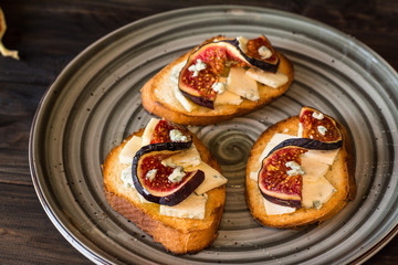 Sandwiches with ricotta, fresh figs, walnuts and honey on rustic wooden board over black backdrop, top view. Bruschetta with figs. Aperitive. Mediterranean cuisine. Crostini.