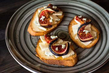 Sandwiches with ricotta, fresh figs, walnuts and honey on rustic wooden board over black backdrop, top view. Bruschetta with figs. Aperitive. Mediterranean cuisine. Crostini.