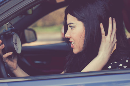 Stressed woman with alarm clock in a car