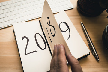 New Year 2019 is coming concept. Female hand flips notepad sheet on wooden table. 2018 is turning,...