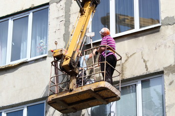 Women plasterers in orange helmet and safety harness on a crane basket repair the facade of a old...