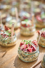 Tasty appetizers with wooden spoons served in glass jars on wooden table.