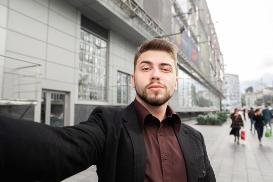 Business man with beard standing against the background of the street and take selfie. Selfie concept.