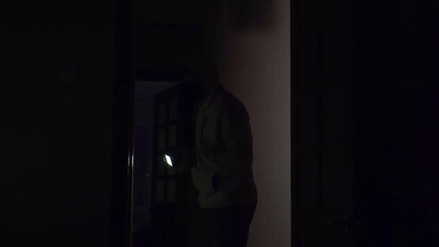 Masked robber with a flashlight in his hand inspects the apartment