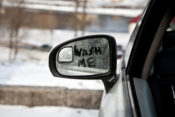 Wash me inscription on the dirty side view mirror of a car, winter time