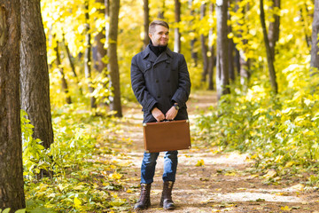 Fall, season and people concept - handsome man standing with retro suitcase in autumn park