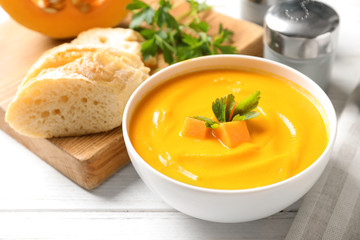 Bowl with delicious pumpkin cream soup and bread on wooden table