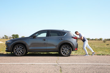 Man pushing broken car along country road