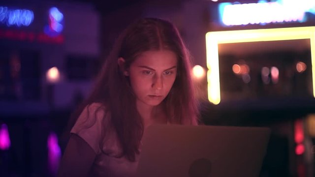 The girl works outside the office with a laptop in the night city