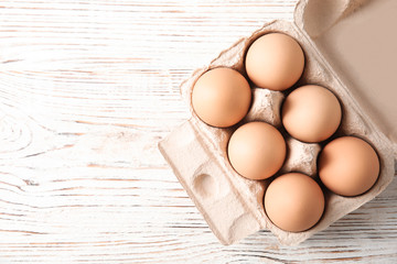 Carton of raw chicken eggs on wooden background, top view. Space for text