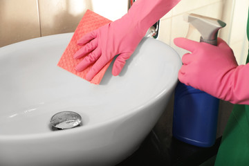 Woman in protective gloves cleaning bathroom sink with rag, closeup