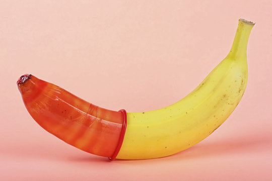 Yellow banana with red condom on a pink background