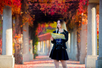 Young girl with map and camera try to find a way. Autumn season alley