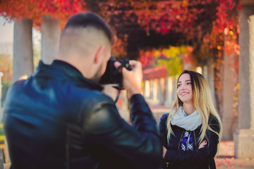 Young photographer making a photo of a beautiful girl in a park. Autumn season time