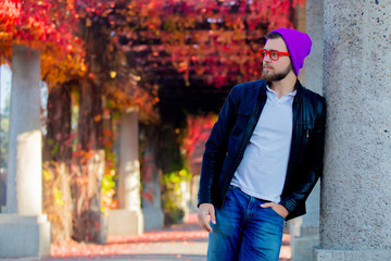Obraz premium Young white guy in glasses and hat in a park with yellow trees on background. Autumn season time
