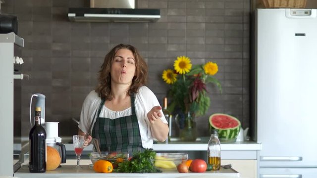 Healthy food. Young sexy woman dances in the kitchen with a knife and tastes the salad. Prepares a salad, great mood. Mothers Day