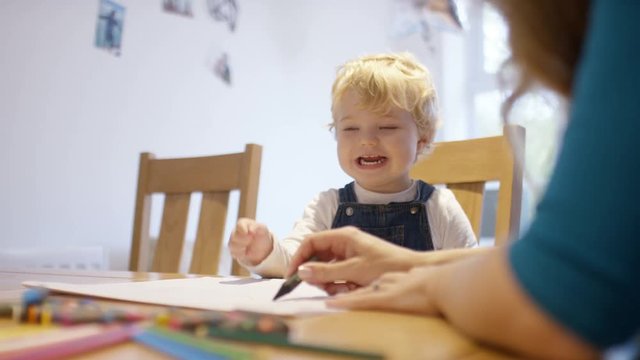Young toddler at the kitchen table drawing with his mother
