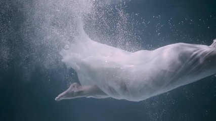 Young beautiful woman in white dress swimming underwater