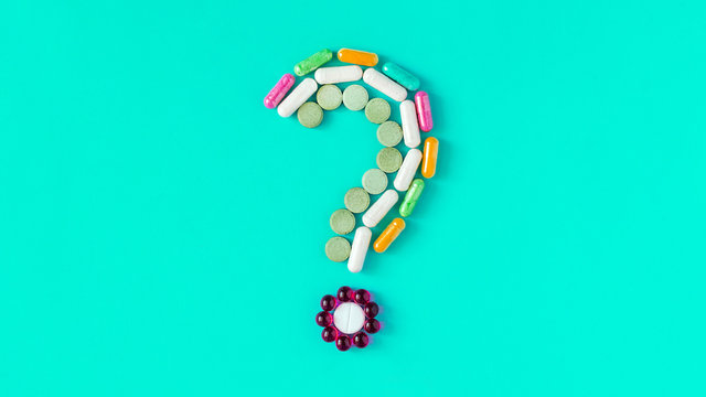 Question mark made of different colored pills, tablets and capsules on blue background. Pharmaceutical industry, and prescription minimal concept