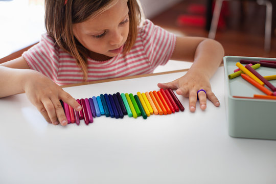A child lines up colorful crayons in a row. 