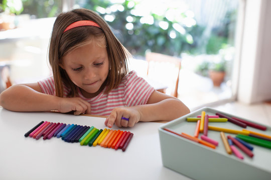 A child lines up colorful crayons in a row. 