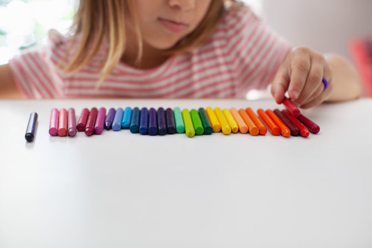 A child lines up colorful crayons in a row. 