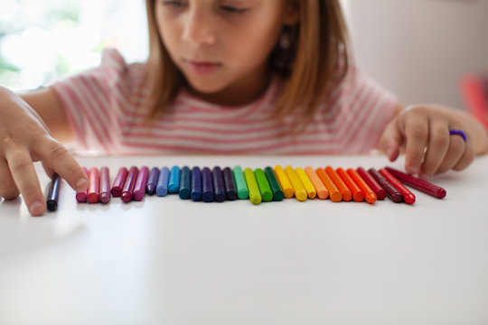 A child lines up colorful crayons in a row. 