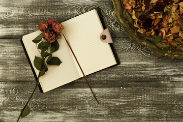 Top view of vintage tray with petals of dried rose flowers and a diary or notebook and dried rose flower on a gray wooden table. Flat design. Copy space.