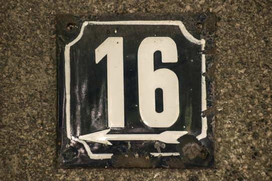 Weathered grunge square metal enameled plate of number of street address with number 16 closeup