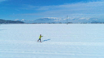 Naklejka premium AERIAL: Flying along an active woman skiing across vast snowy plain in Slovenia.