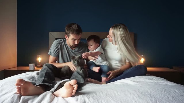 Family of three sit on the bed with 1 years child girl and cat